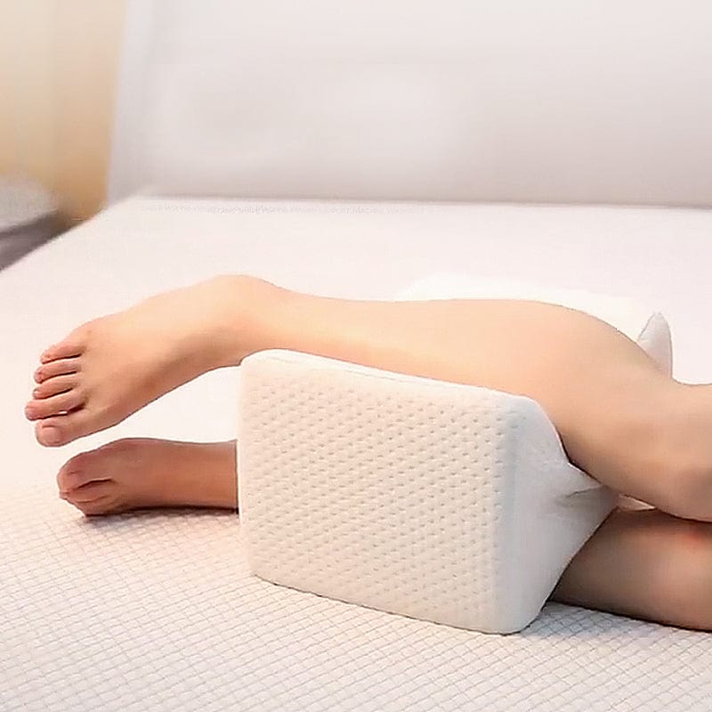 Person using a white leg elevation pillow on a bed